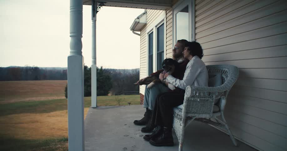 Couple sitting on porch at remote country house petting thier dog