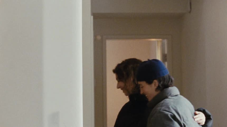 Woman smiles while letting her friend zip up her coat then puts an arm around the other woman as they leave