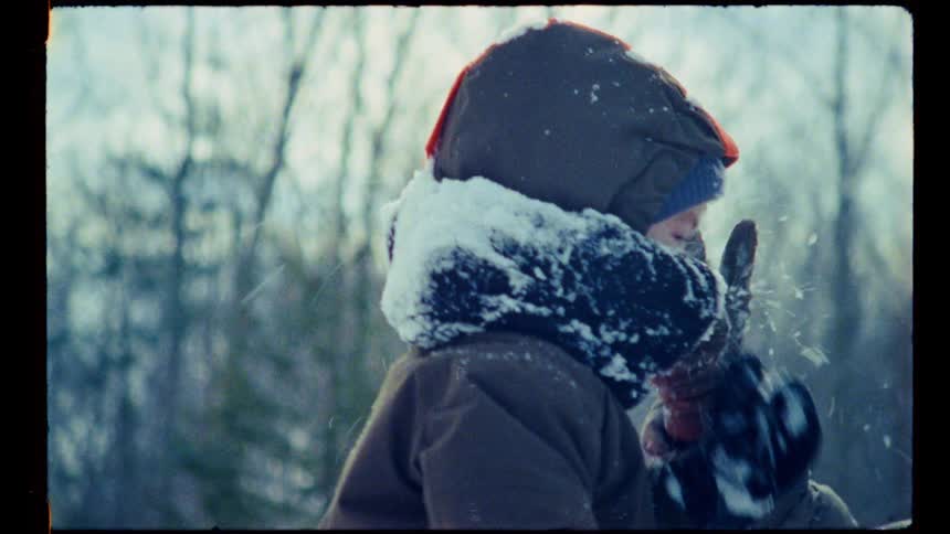 A mother plays with her child packing snow on his head on a winter day both dressed in heavy winter clothing