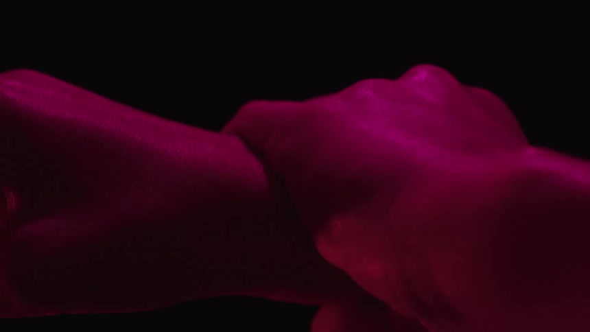 Two hands hold each other under intense red lighting