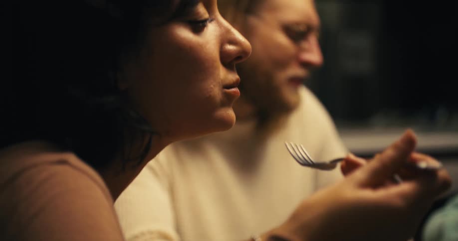 A family are seated at a table and the woman is eating with a fork while the man is talking with a third person