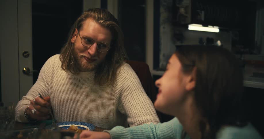 Longhaired man with glasses eating a meal at the table beside a young girl