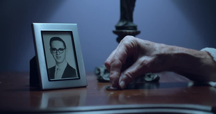 A persons hand places a ring on a table next to a framed black and white photograph and a lamp