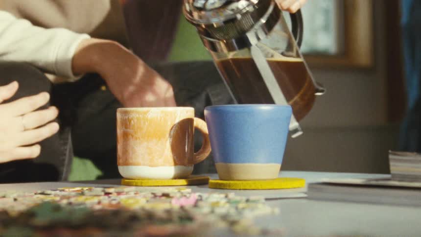 Pouring coffee from a percolator into yellow and blue mugs