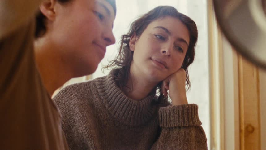 A woman with curly brown hair and a man with a cap on are talking the woman is resting her chin on her hand while she is talking to the man