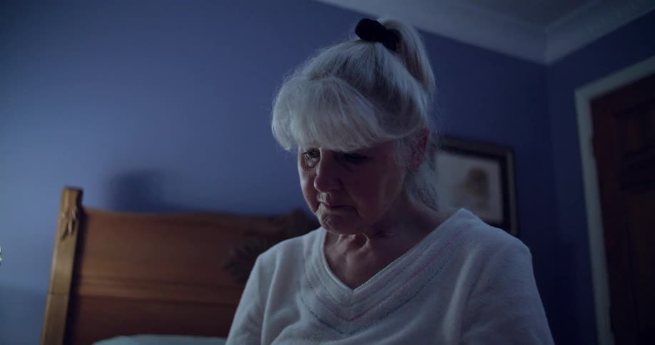 Elderly woman sitting in the bedroom with a serious expression