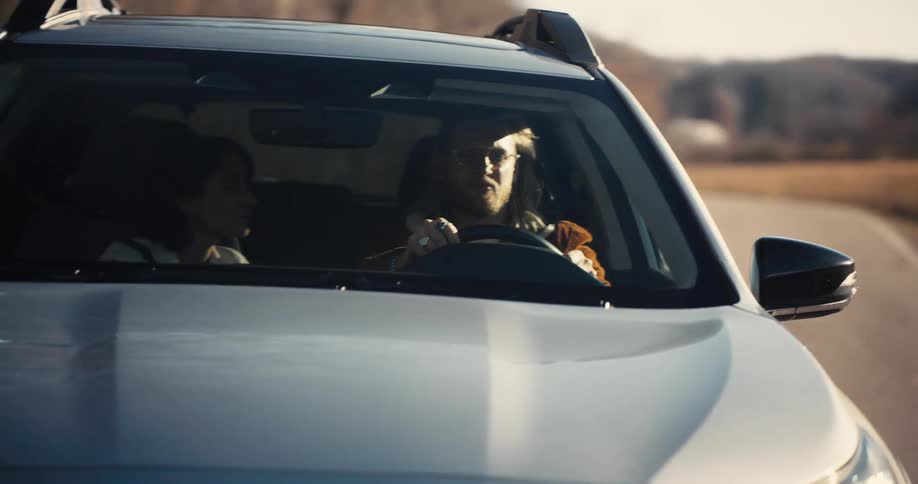 Man driving a car with a passenger beside him on a sunlit road