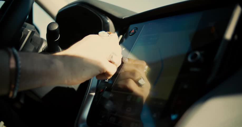 Close up of a driver turning the volume button beside a car monitor while driving during daytime