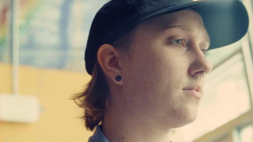 A teenage boy wearing a baseball hat nose ring and earrings is indoors