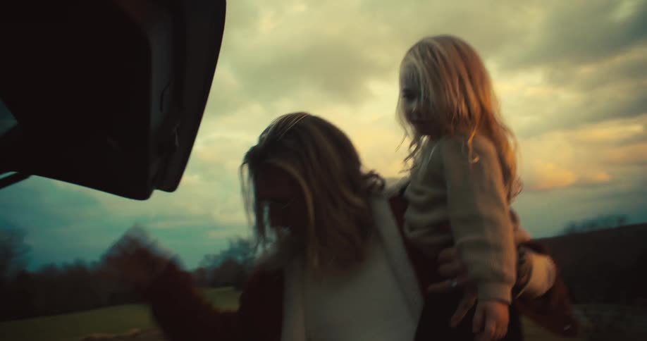 Father picking up his little daughter and taking an object from the trunk of the car