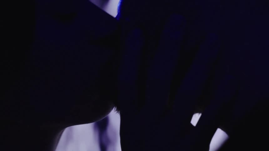 A very close view of a man and a woman in silhouette shows them kissing in profile with their hands reaching toward each other as a bright blue light passes over their bodies