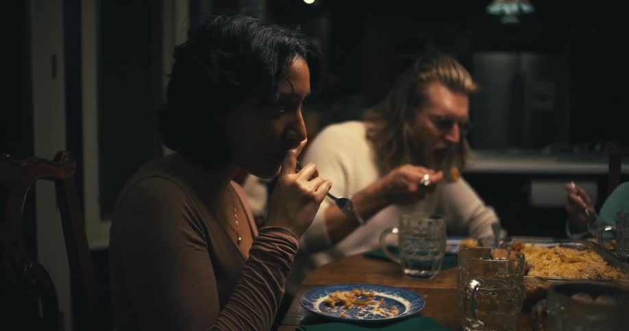 A man a woman and a girl in a lowlight intimate setting sharing a meal and a conversation at a dining table