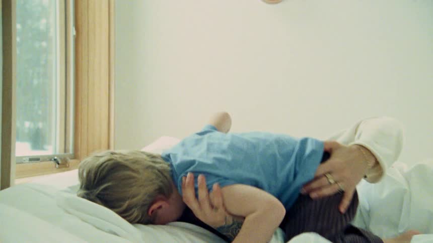 A mother and son cuddle and play joyfully on a bed