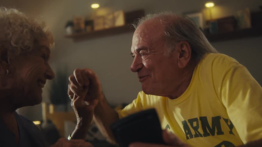 Elderly couple clasps hands and hugs while smiling after viewing the information on a smartphone