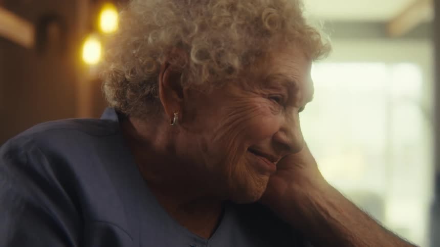 An elderly woman has a warm smiling conversation indoors
