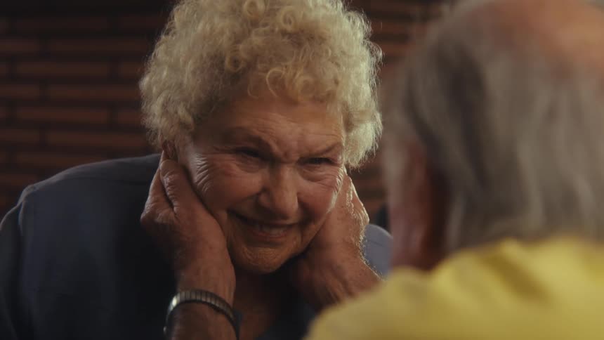 Smiling elderly woman being caressed on the face by a man