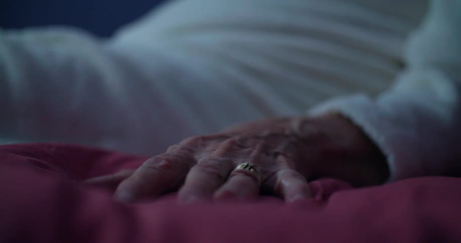 Elderly hand with a gold ring rests on a red blanket