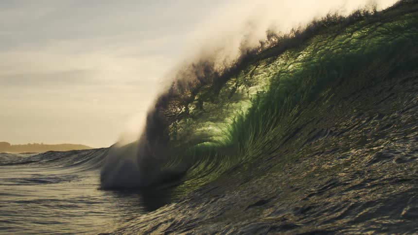 The ocean forms a huge wave crashing into the water at sunset