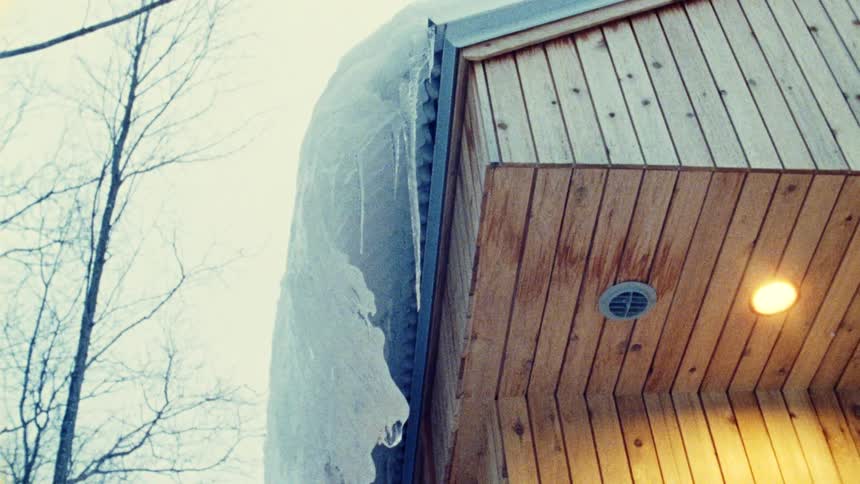 Thick layer of ice covers the roof of a wooden house with a light turned on