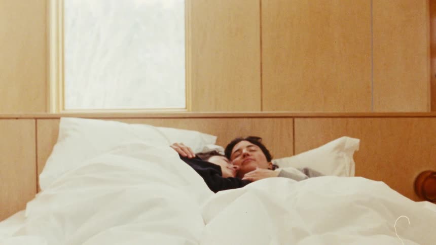 A couple sleeps cuddling in bed in their bedroom at sunrise