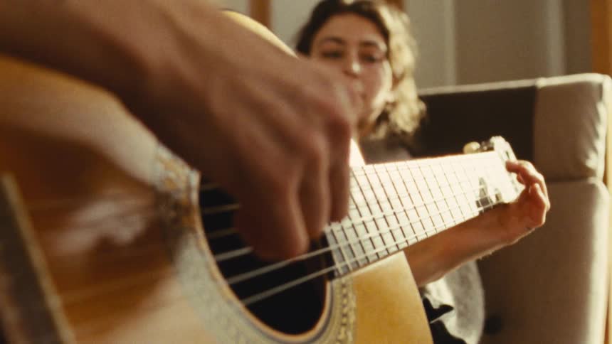A man plays acoustic guitar while a woman listens and watches him play