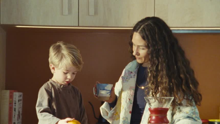 Woman and child in a brightly lit kitchen with fruits and coffee on the counter