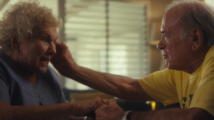An elderly couple shares a tender moment holding hands