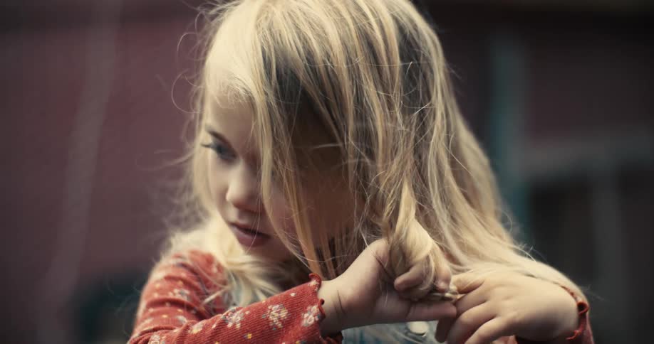 A young girl looking very focused as she twirls her long blonde hair around her fingers