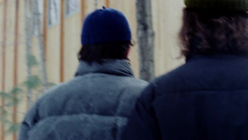 Two people in coats and beanies seen from behind walking in a snowy area
