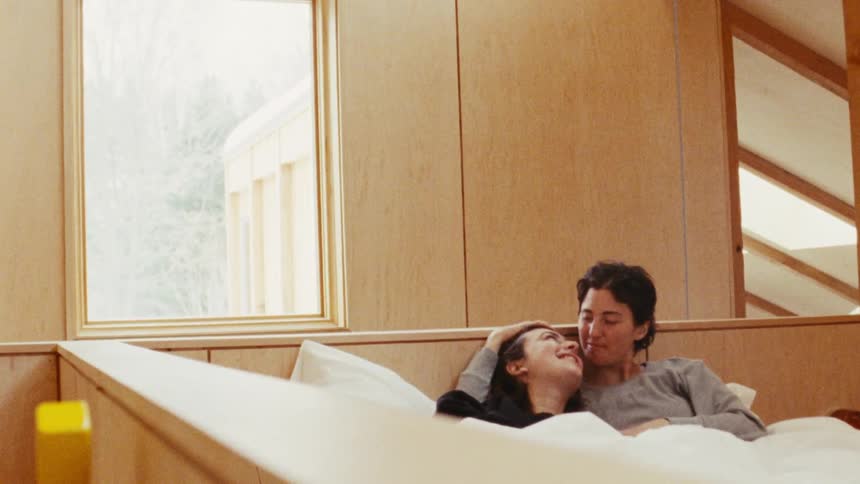 The video shows two people lying in bed together with one person gently stroking the others hair the scene has a calm and tender atmosphere with soft natural light coming from a nearby window