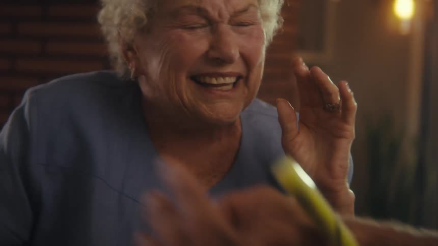 A closeup of an elderly womans smiling face shows her talking to someone with a joyful expression