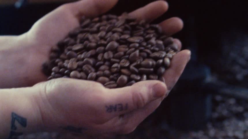 Person scooping coffee beans in palm of thier hands from a large container