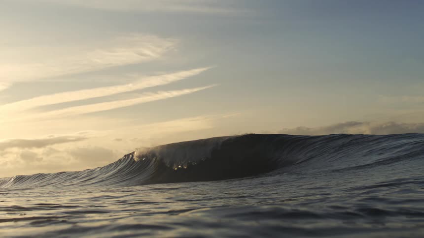 A small ocean wave rolls gently under a golden sky at sunrise or sunset