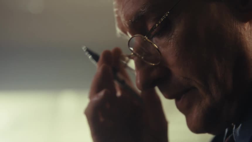 The video shows a side profile of a persons head and face with light reflecting off their glasses they are smiling or laughing as indicated by the expression on their mouth