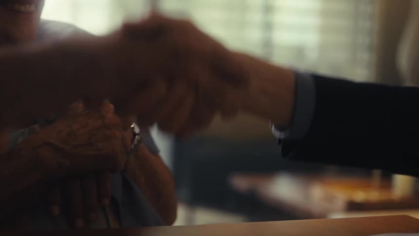A close view of a handshake between three people is shown with the person on the right wearing a suit jacket