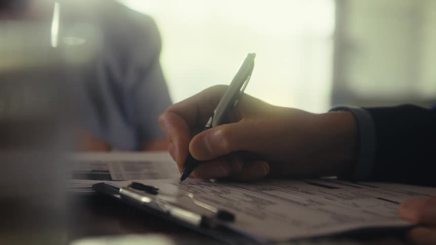 A person fills out paperwork as a medical professional stands nearby