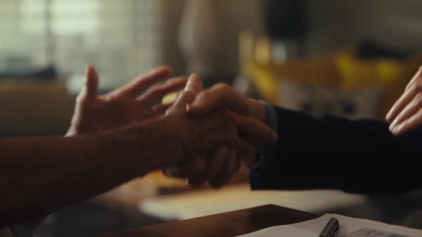 A handshake over a table a pair of hands from an old man and the other from a younger man