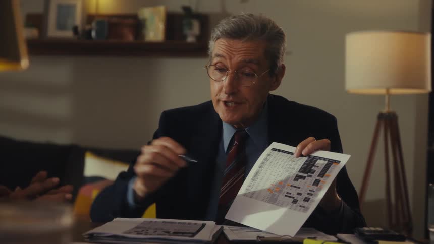 An older man holding a paper and pointing with a pencil showing and explaining something