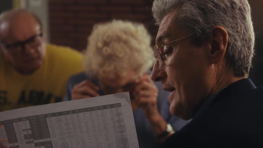 An elderly couple looking at a document held by a man in formal attire who is explaining its contents