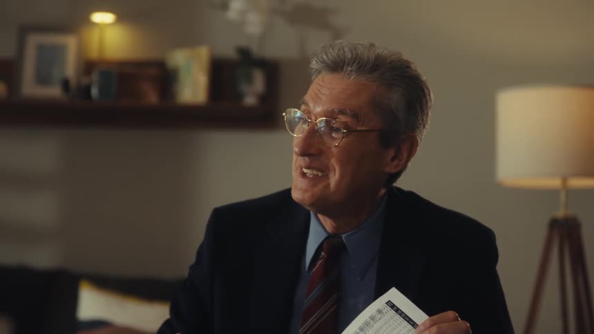 Man in suit and glasses points to a printed chart during explanation