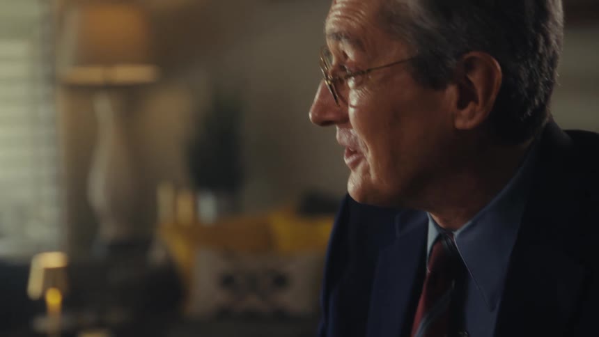 Man in a suit and glasses talking indoors
