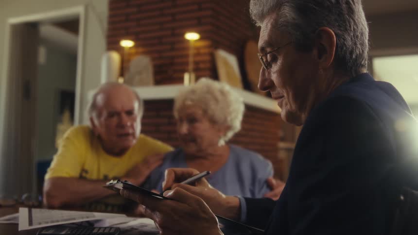 Three people sit as a man explains documents on a clipboard