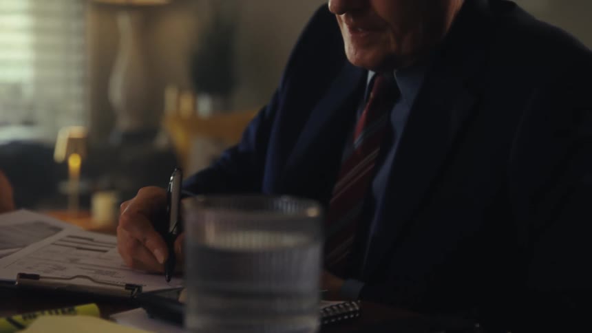 A man in a suit is writing on documents at a desk