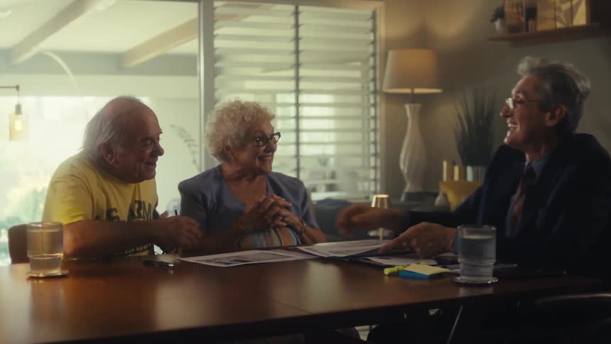 Three peopletwo elderly and one professionalsitting at a table and engaging in a positive discussion that culminates in a handshake