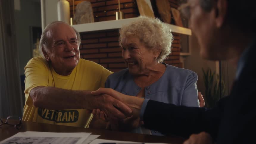 A married couple sit at a table across from a financial advisor with the advisor shaking hands with the woman then the man as the couple smiles