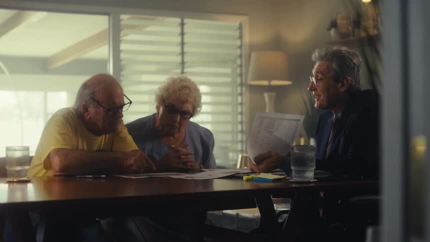 Older businessperson goes over documents with his elderly clients while sitting at a table
