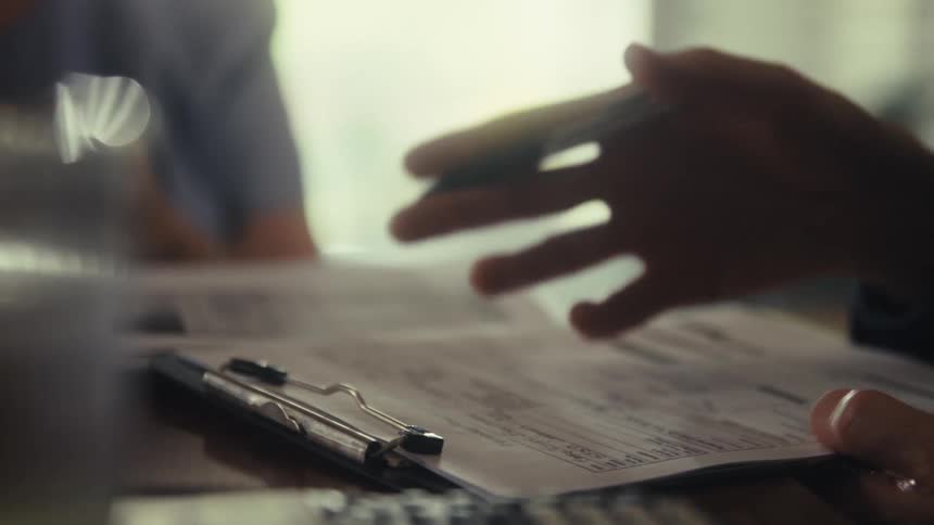 A hand with a pen between its fingers moving over a paper form
