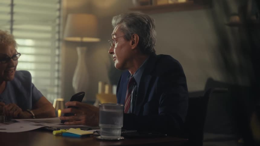 Older businessman uses his smartphone to illustrate a point while talking to an elderly woman