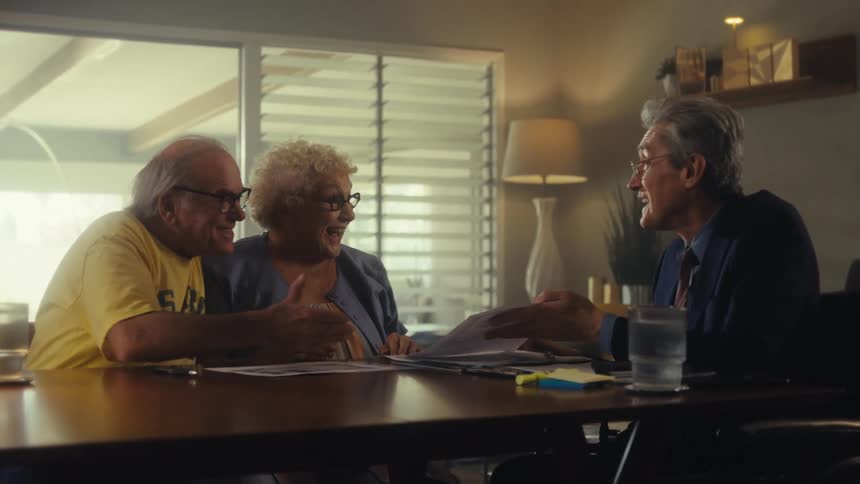 An elderly couple looking at a document shown by an older man in formal attire the couple happy to receive the news