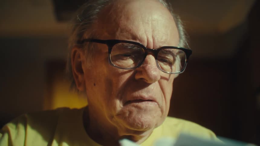 A man wearing glasses and a yellow us army veteran tshirt is sitting at a table he holds a stack of papers and appears to be intently reading them
